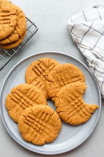 Peanut butter cookies on a gray plate with a bite taken out of one cookie and a few more nearby on a wire rack.
