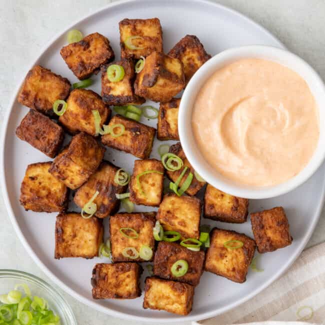 Large serving platter with tofu along with small dipping bowl for spicy mayo with lime wedges nearby and garnished with sliced scallions.