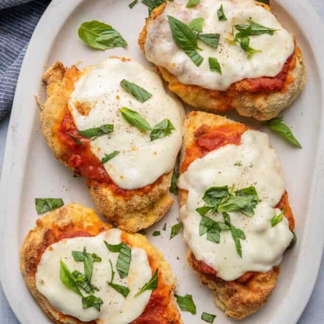 Chicken parmesan on a plate topped with melted mozzarella cheese and basil