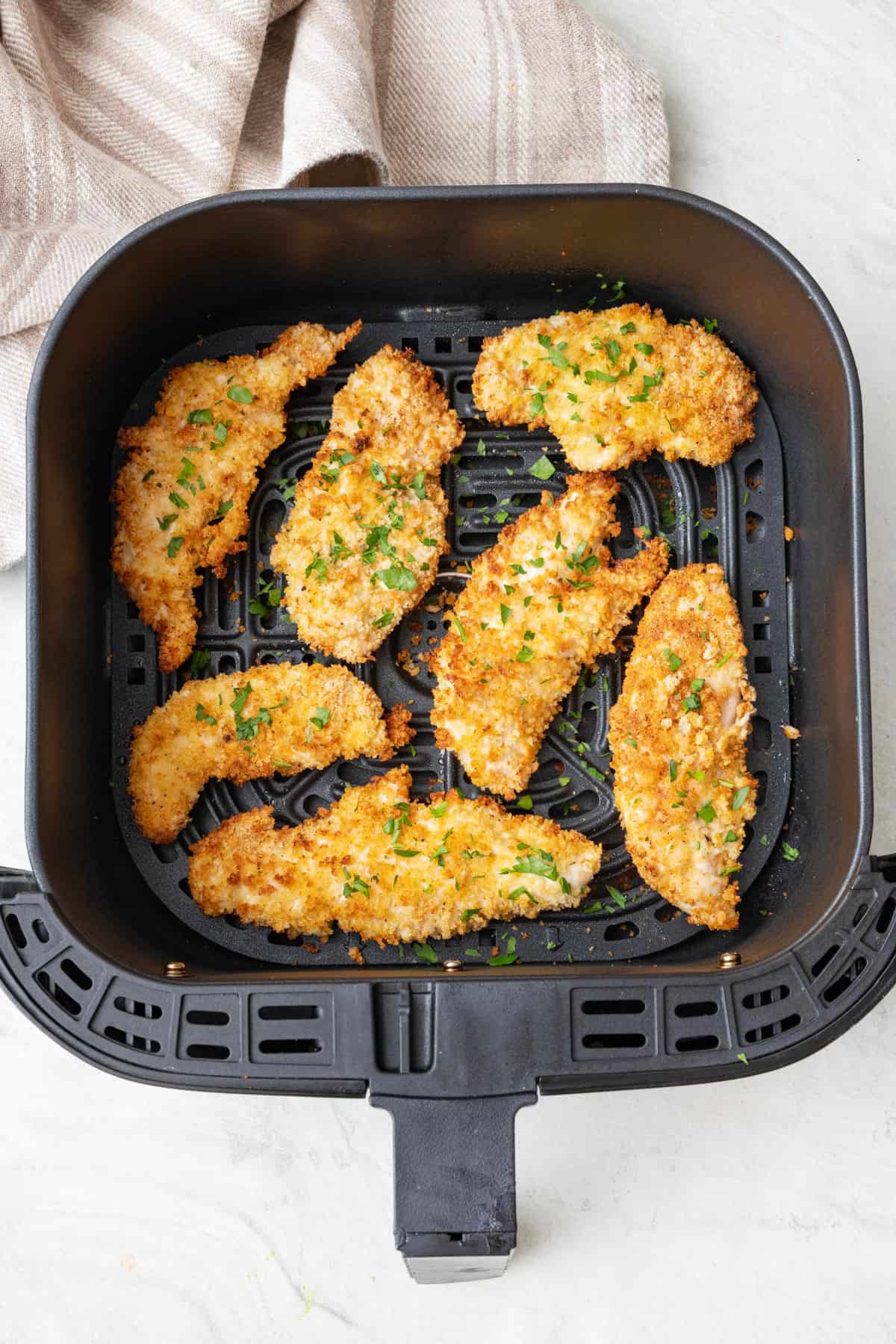 Air fryer chicken tenders in an air fryer baskets garnished with fresh chopped parsley.