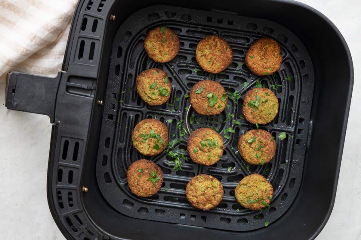 Falafel balls in air fryer basket garnished with fresh parsley.