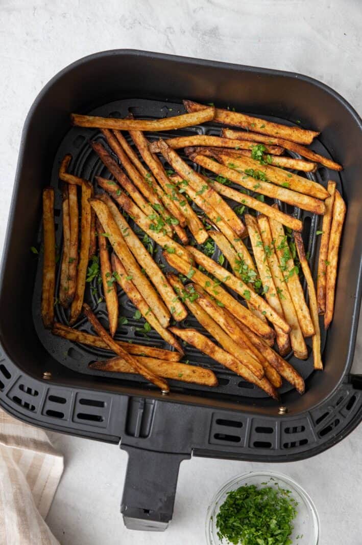 Fries in an air fryer basket garnished with fresh parsley.
