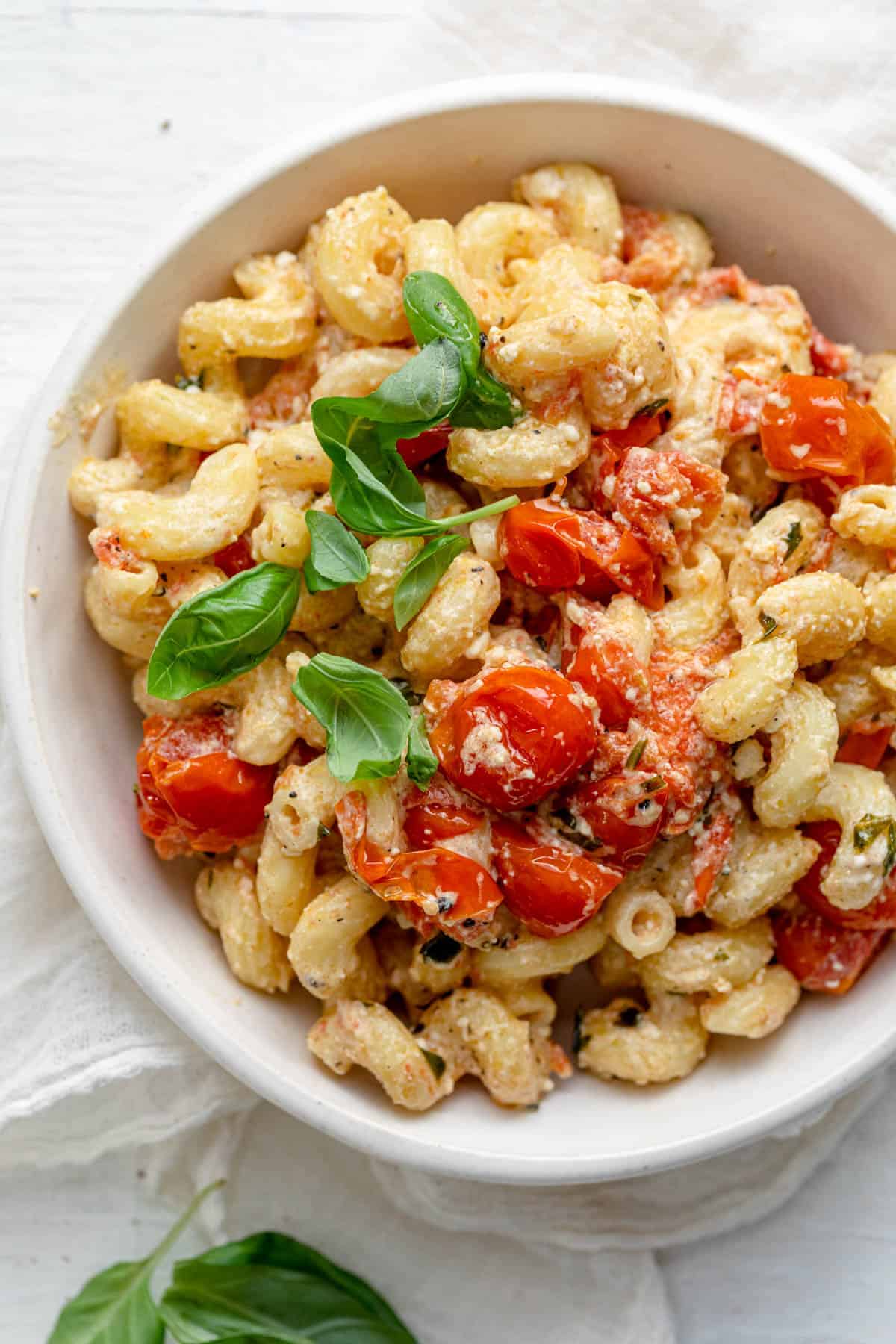 Large bowl of baked feta pasta topped with cherry tomatoes and basil