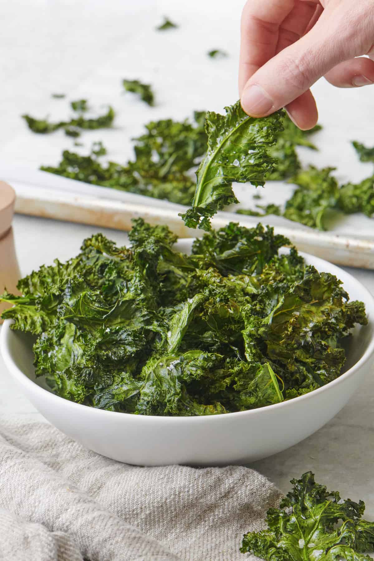 Large bowl of baked kale chips with one getting removed by hand