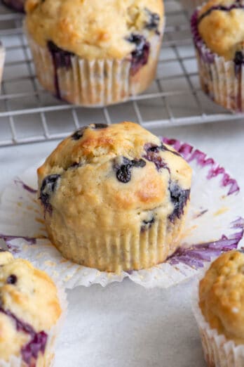 Close up of a single blueberry banana muffin with cupcake liner peeled off and more muffins around it.