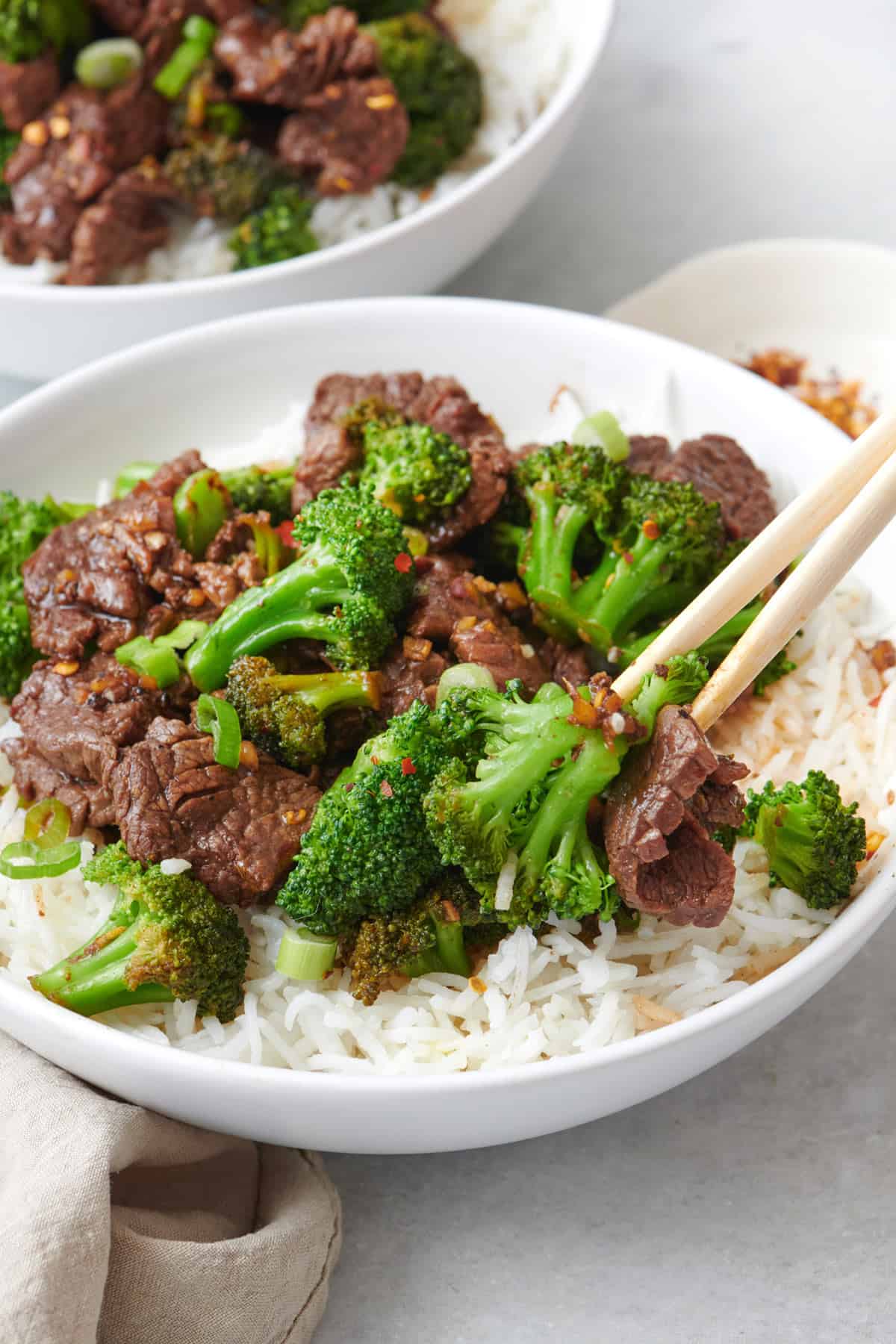 Close up shot of a large bowl of beef and broccoli rice with chopsticks on the side