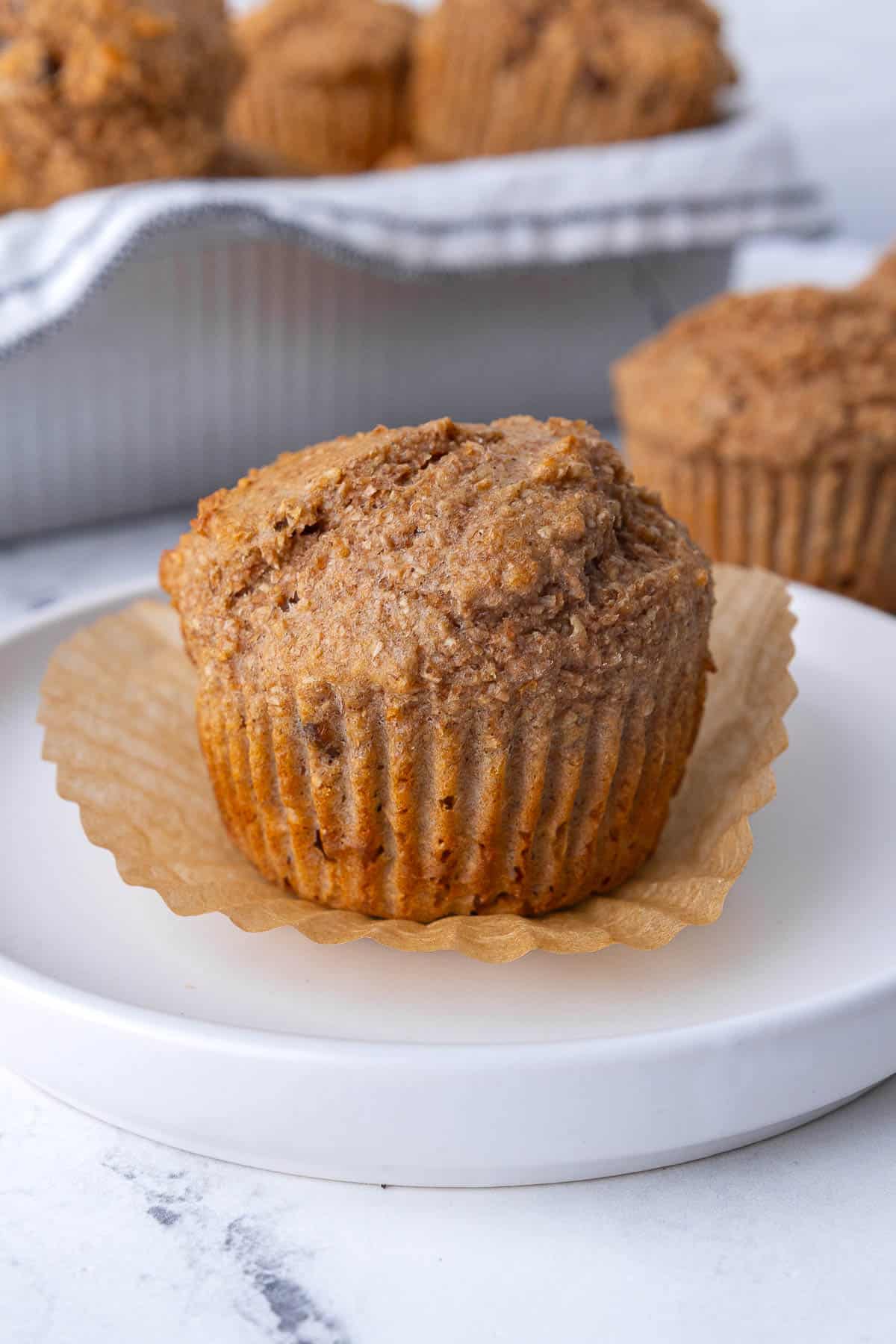 Bran muffin on a plate with the paper peeled away.