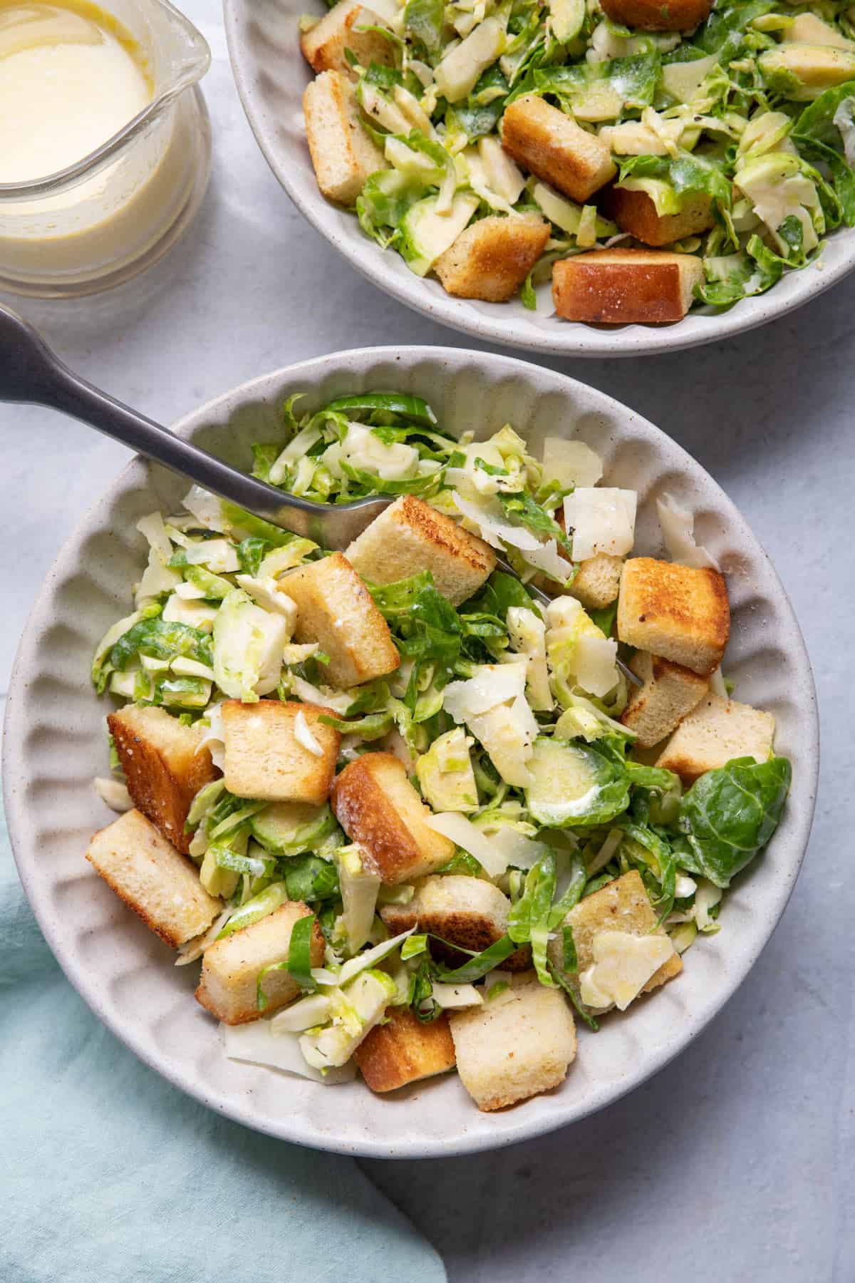 Two small bowls of the brussel sprout salad with croutons and dressing on the side