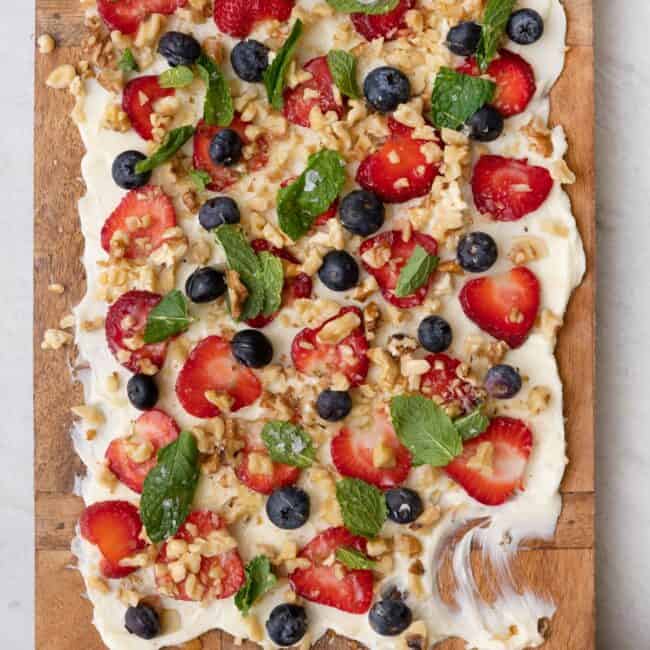 Butter board topped with fruit, nuts, and mit with some smeared off and a few slices of bread nearby.