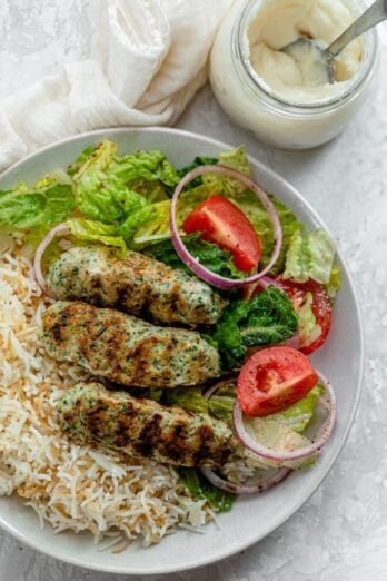 Chicken kafta on a plate with rice and salad along with garlic sauce on the side