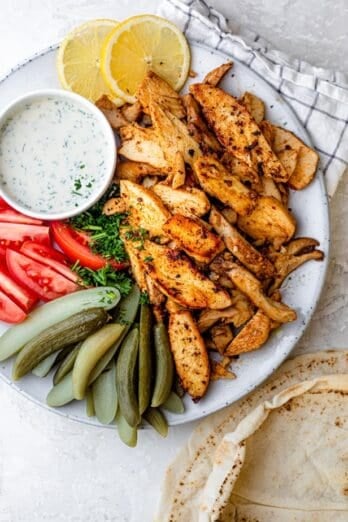 Chicken shawarma on a white plate with sliced vegetables and pickles