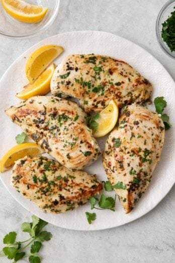 Cilantro chicken breast on a plate with extra fresh cilantro and lemon wedges.