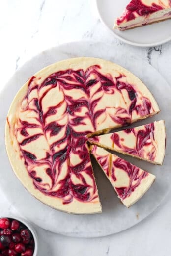 Cranberry swirl cheesecake with a few slices cut and one piece being pulled away.