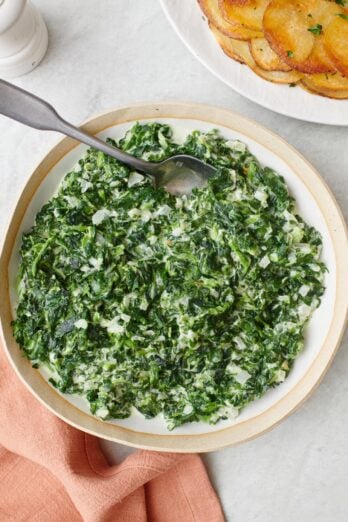 Creamed spinach in a serving bowl with a spoon dipped inside.