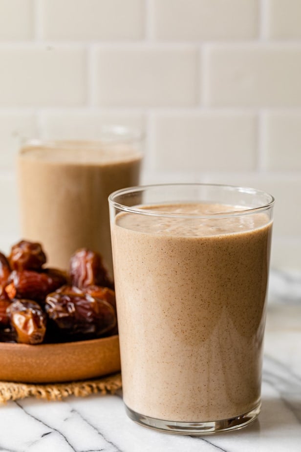 A date shake in a glass in front of a plate of dates