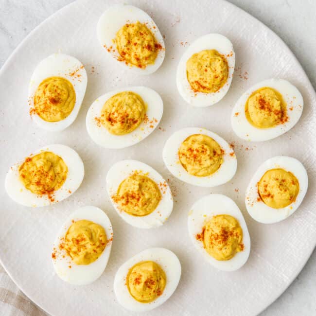 Plate with 12 deviled eggs sprinkled with paprika.