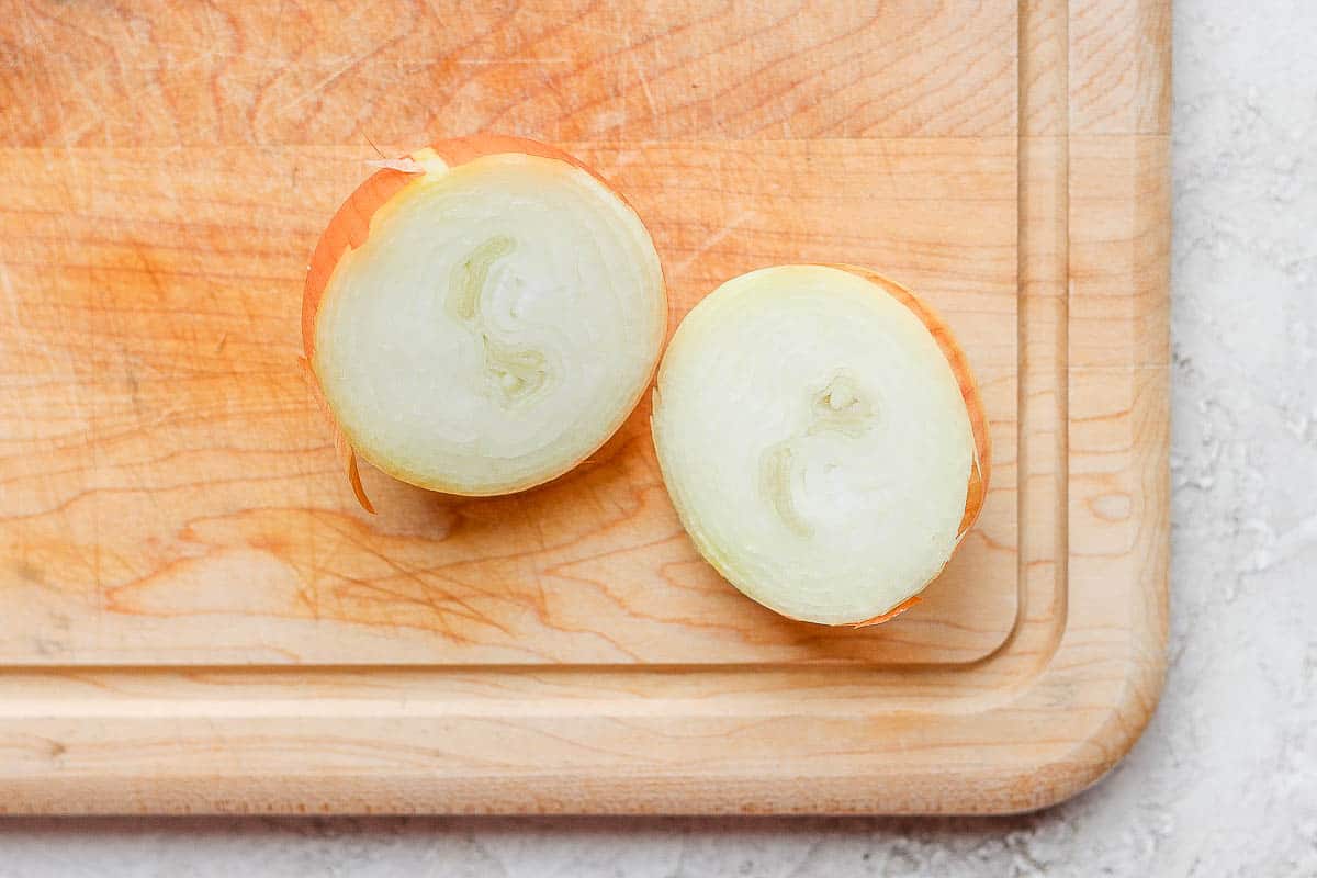 Yellow onion cut in half on cutting board.