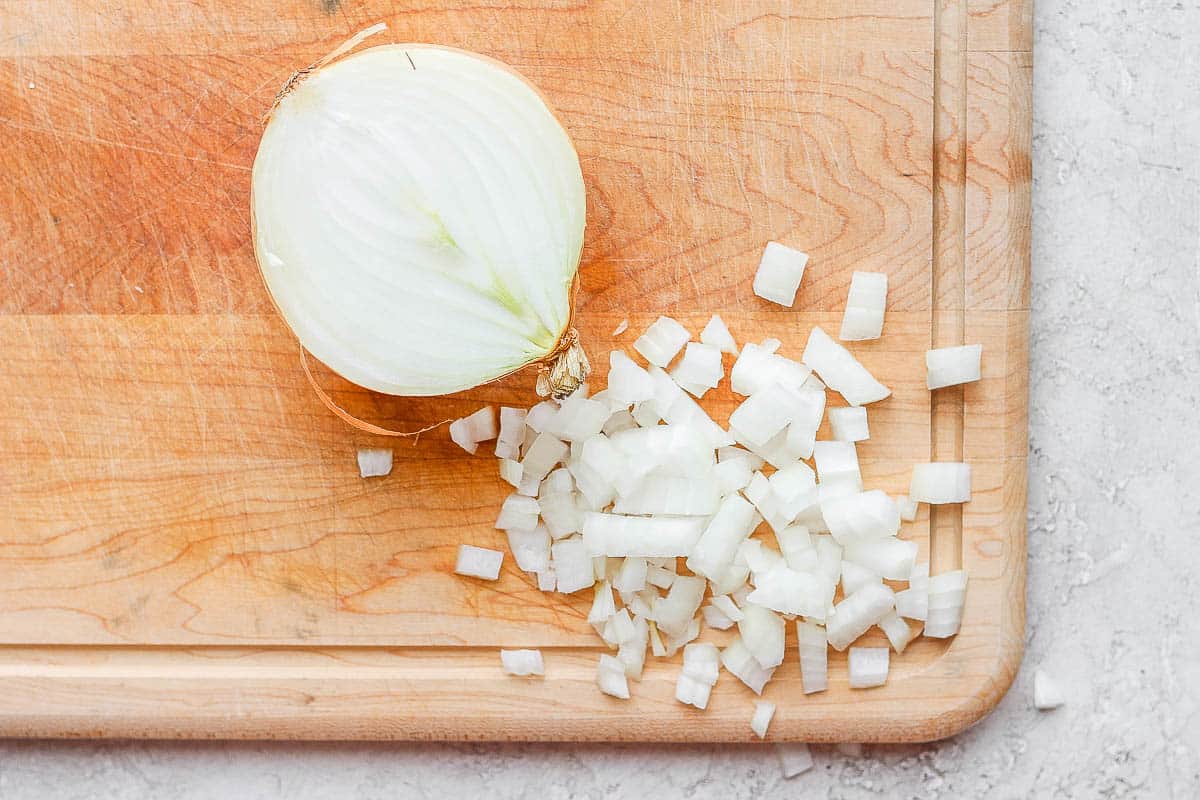 Sweet onion cut in half and then half of it diced on a cutting board.