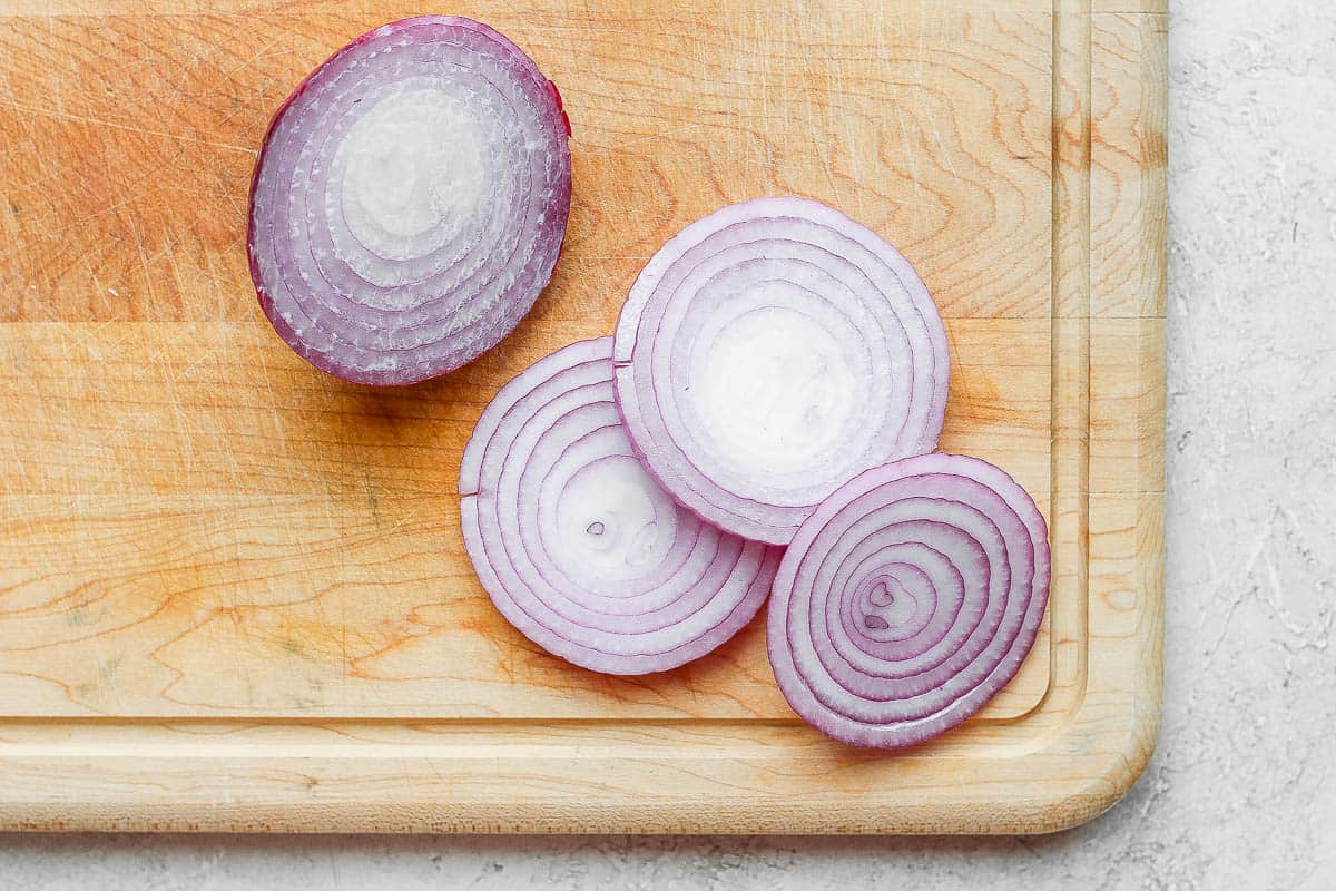 Red onion sliced into rings on cutting board.