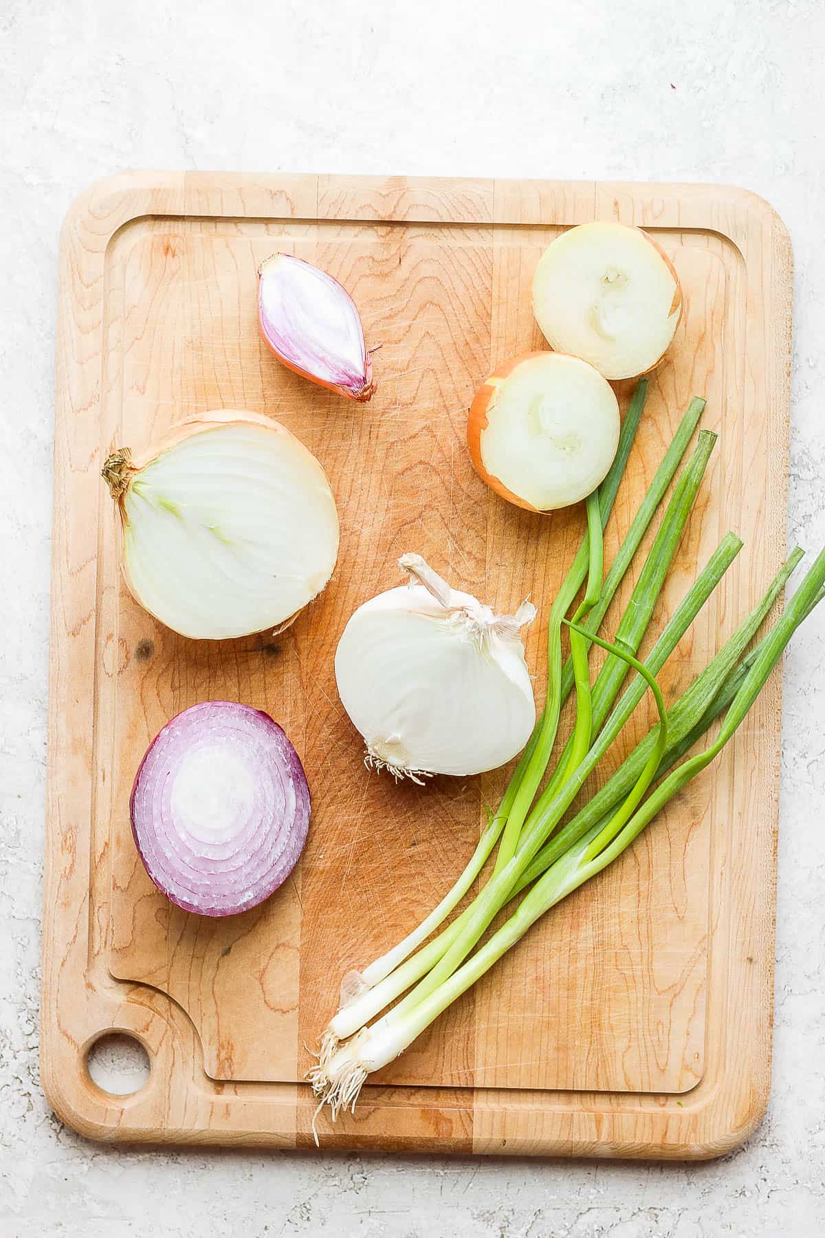 Cutting board with 6 types of onions cut in half.