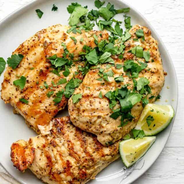 Plate of grilled chicken made with dijon marinade and served with lime wedges and cilantro