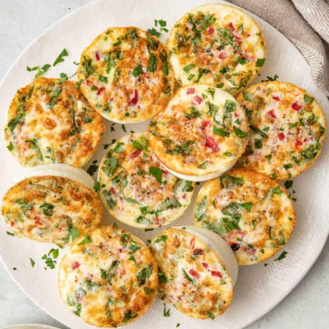 Egg white bites on a plate with 2 on a smaller plate nearby, garnished with fresh parsley.