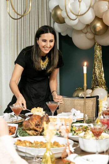 Yumna standing at the Thanksgiving dinner table with dishes of food around and holiday guests enjoying their meal.