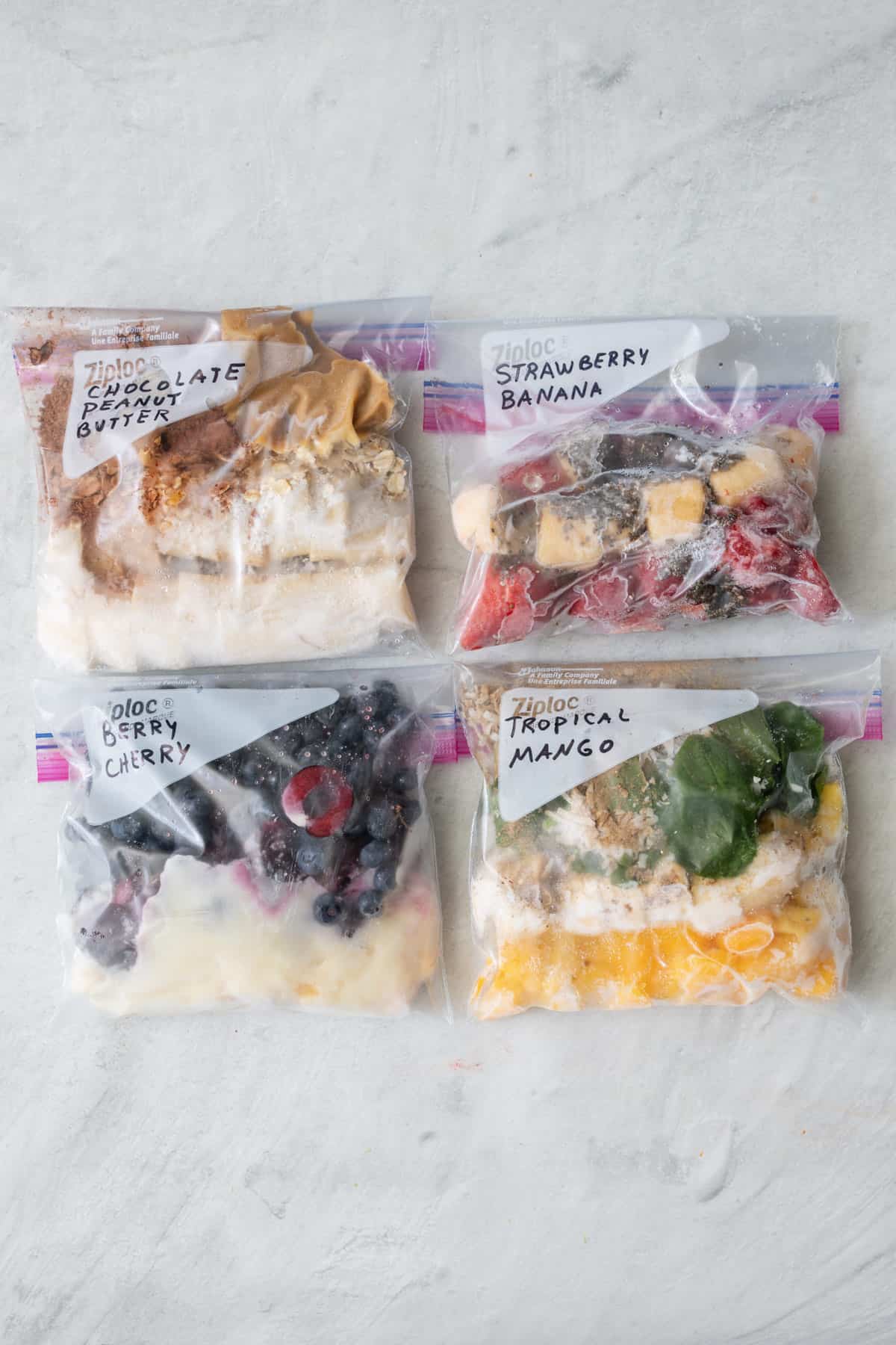 4 zip top bags with different smoothie recipe ingredients in each after being frozen.