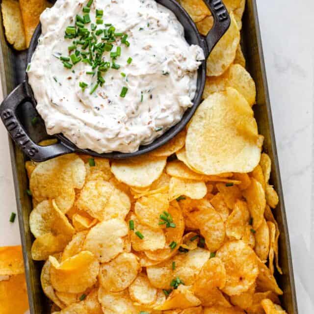 Homemade french onion dip in a small bowl with potato chips around it in small tin