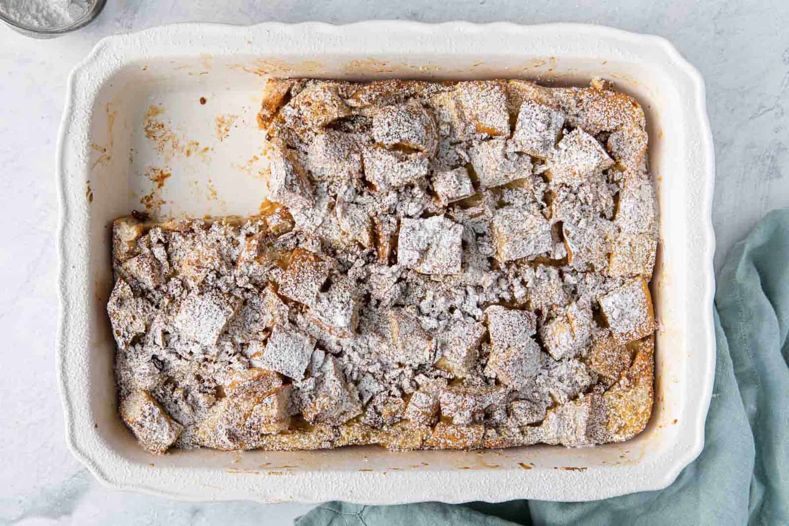 French toast casserole served in baking dish dusted with powdered sugar and a slice removed.