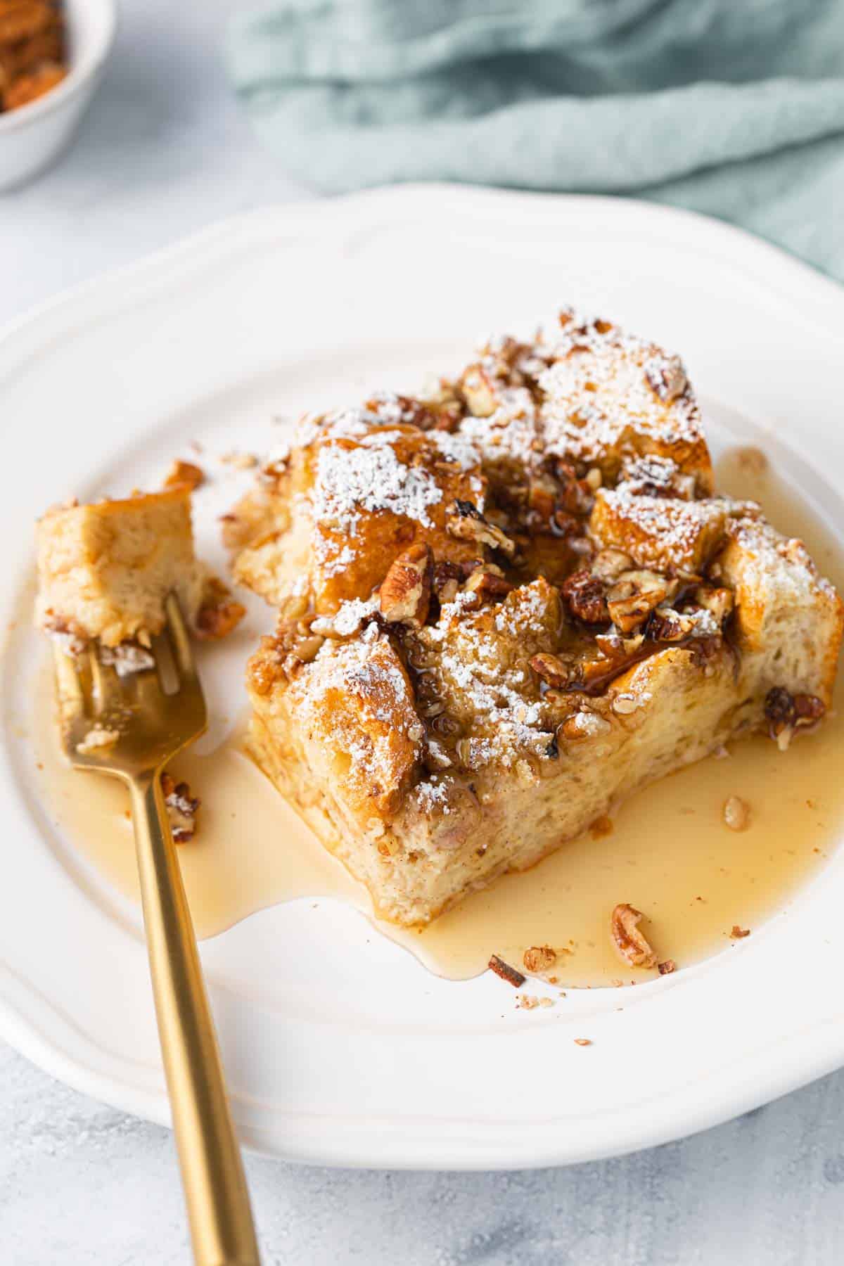 A slice of french toast casserole covered in syrup with a fork sitting on plate with a piece on it.