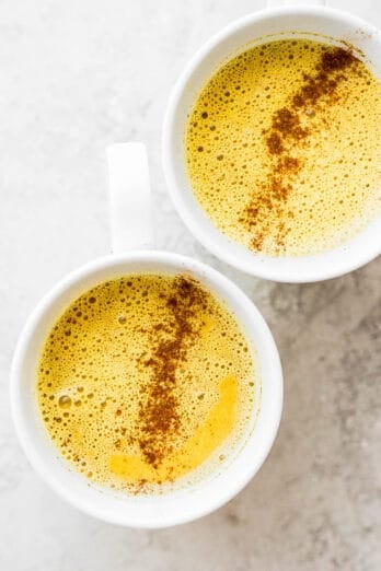 Top down view of the two mugs of golden milk turmeric latte with spices on top