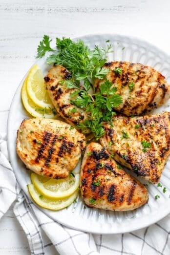 Grilled Lemon Chicken breasts on a plate with lemons and parsley