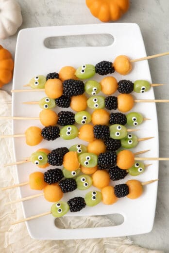 Halloween fruit kabobs on a platter, made with grapes, blackberries, and cantaloup.