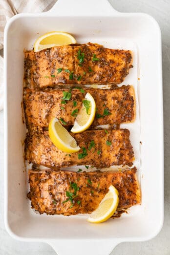 Honey mustard salmon fillets in a large rectangular baking dish, garnished with lemon wedges and fresh parsley.