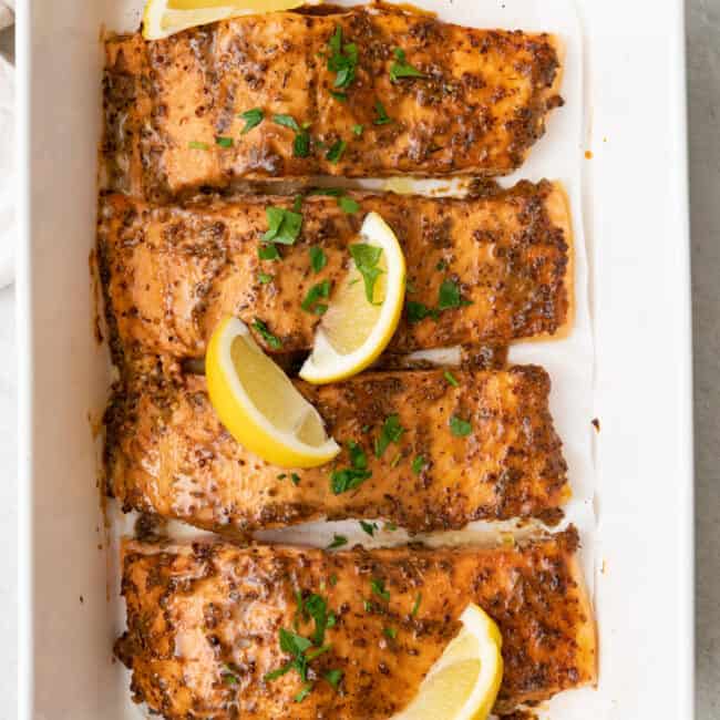 Honey mustard salmon fillets in a large rectangular baking dish, garnished with lemon wedges and fresh parsley.