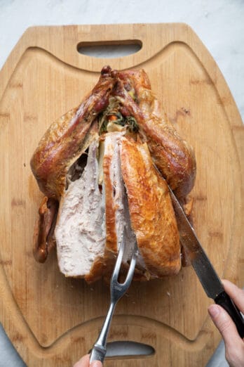 Carving turkey breast on cutting board with carving knife and meat fork
