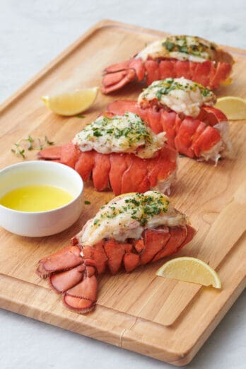 Lobster tails on a cutting board cooked 4 different ways: baked, air fried, steamed, and grilled.