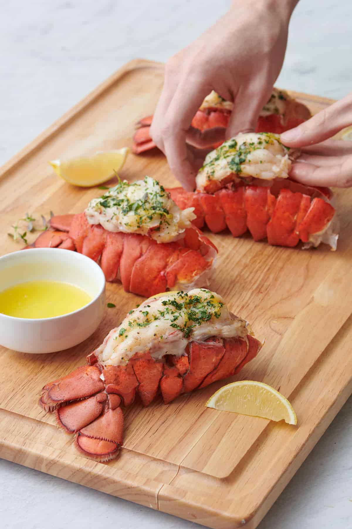 Lobster tails on a cutting board with a hand lifting up the meat from one.