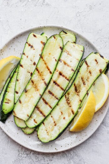 Grilled zucchini slices on a plate with lemon wedges