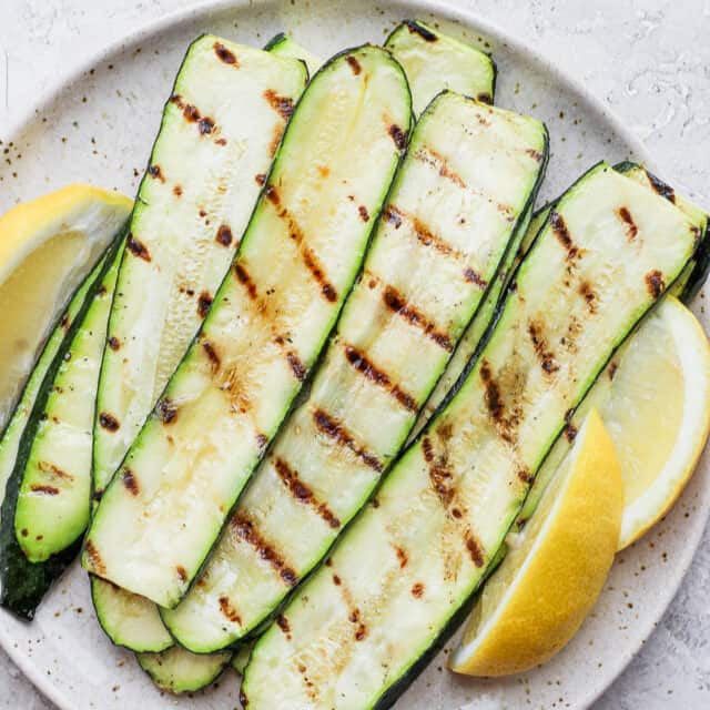 Grilled zucchini slices on a plate with lemon wedges
