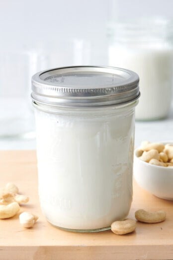 Homemade cashew milk in a mason jar with a small dish of whole cashews nearby.