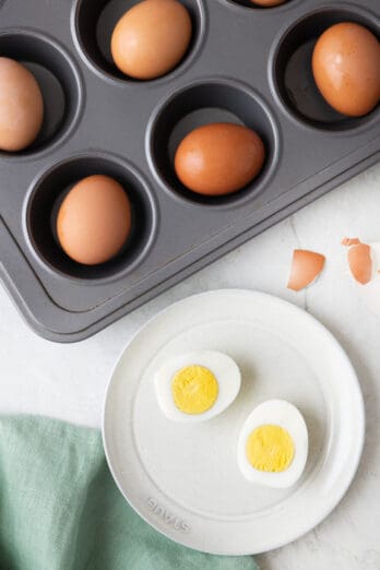 Hard boiled egg on a plate cut in half with muffin pan of more eggs nearby.