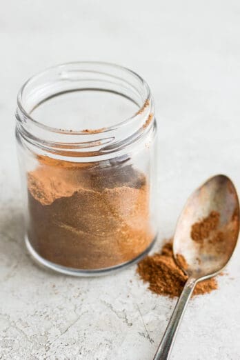 Pumpkin spice in a small jar with a spoon and spice next to it.