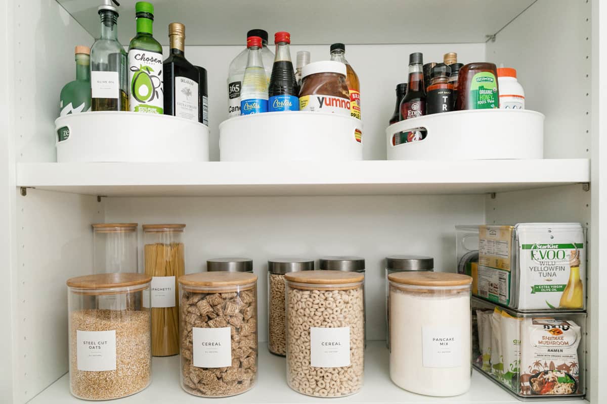 Two shelves in a pantry with pantry staples for sauces, oils, cereals, tuna, and other dry ingredients.