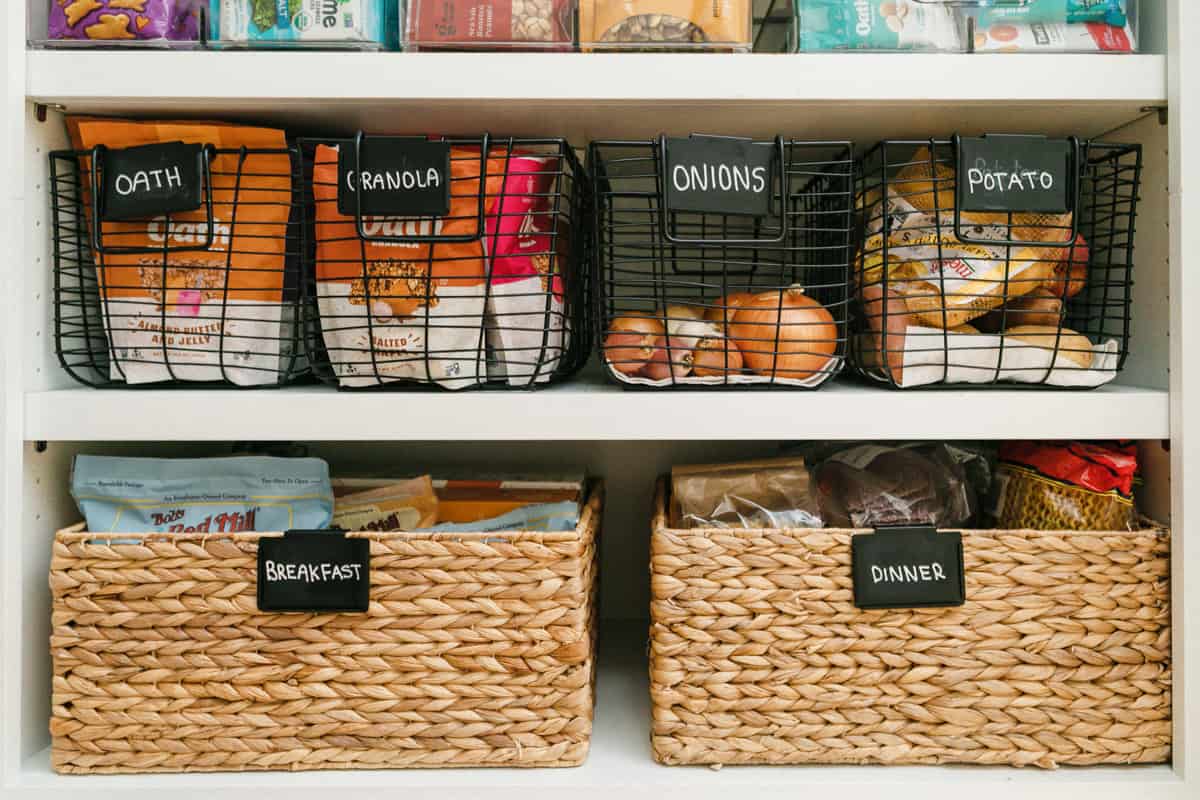 Two shelves in a pantry with pantry staples such as Oath Oats granola, produce like onions and potatoes, plus boxes for breakfast and dinner staples.