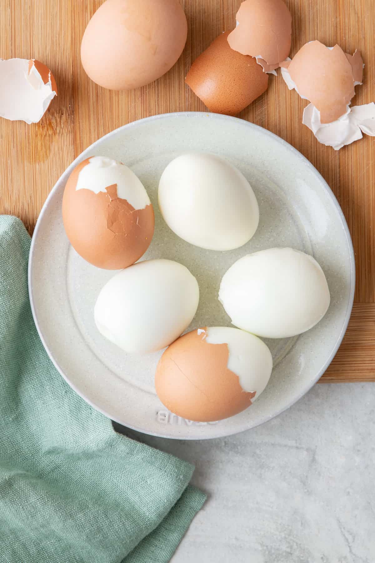 Peeled and partially peeled boiled eggs on a plate next to removed shells.