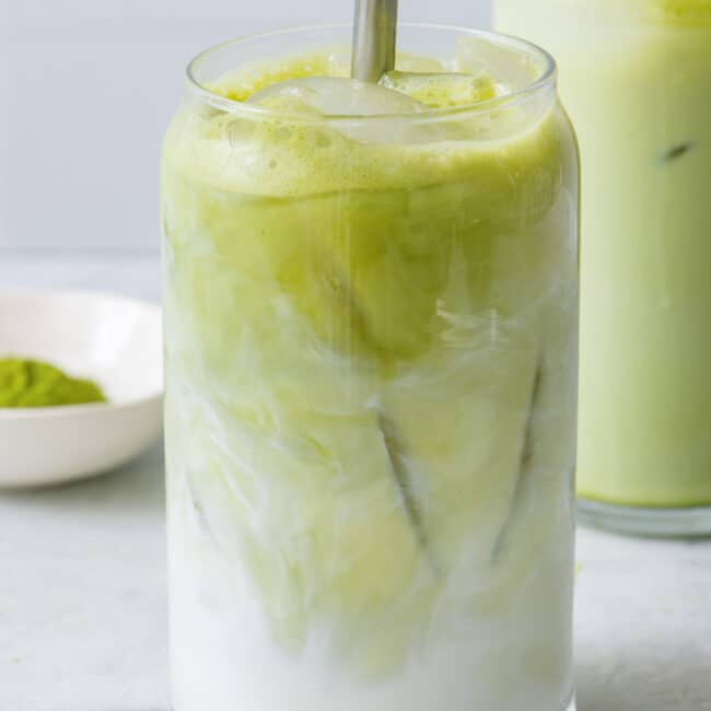 Straw stirring latte layers together in a glass filled with ice.