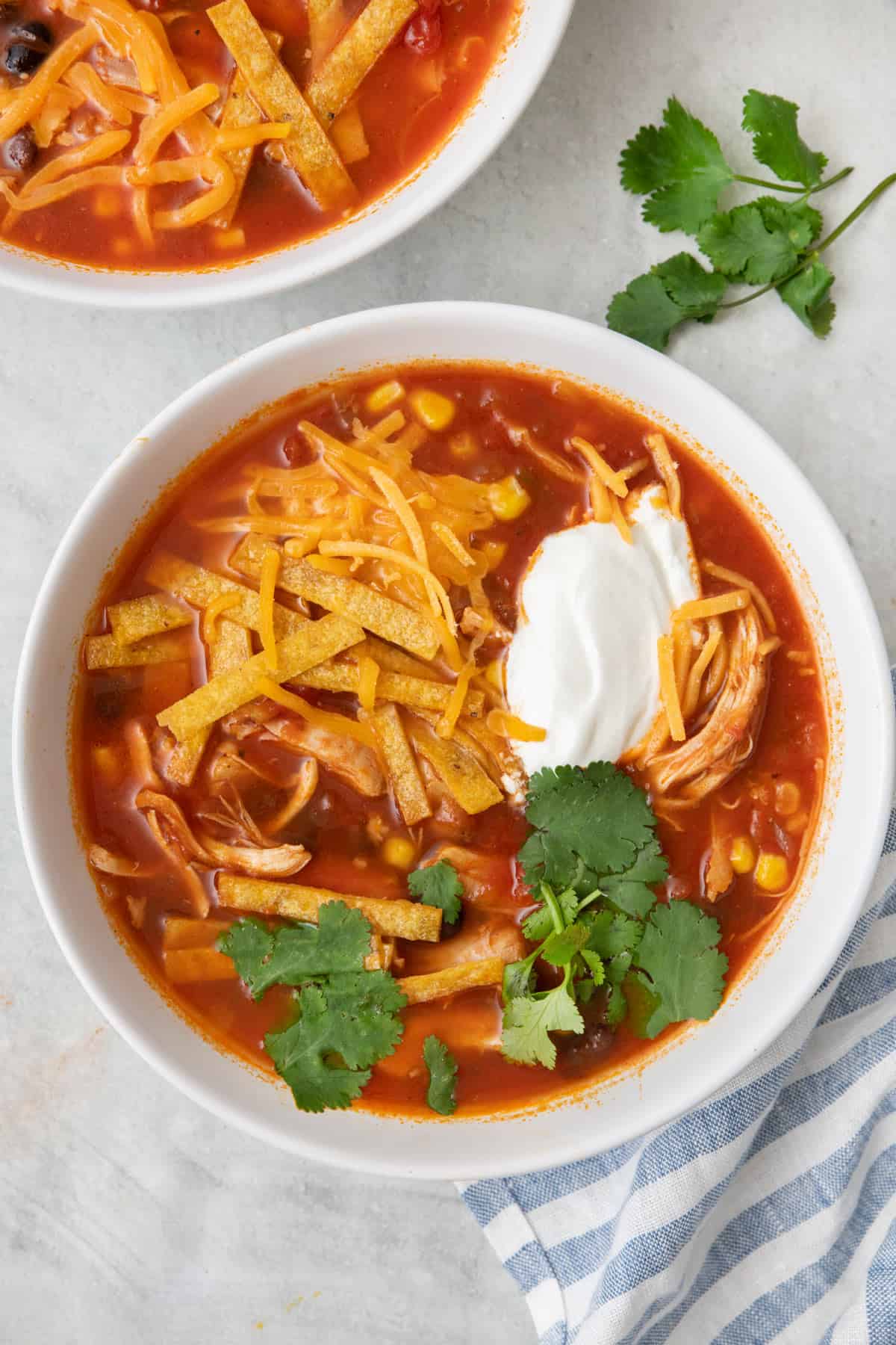 Instant Pot chicken tortilla soup in a bowl, garnished with tortilla strips, sour cream, cheese, and fresh cilantro with another bowl nearby.