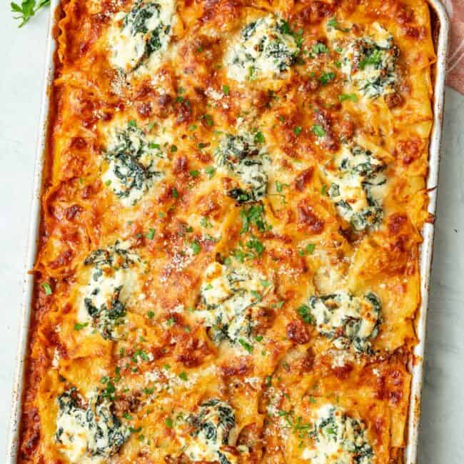 Baked layerless lasagna on sheet pan garnished with fresh parsley and extra grated parmesan.